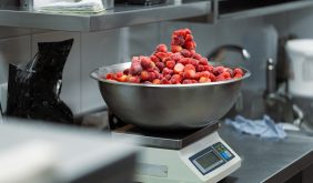 Frozen berry in a bowl on a culinary scales in kitchen