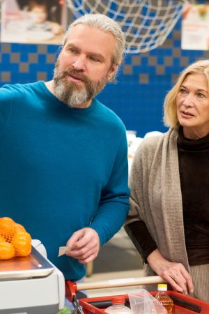 Mature male customer pressing button on display of electronic scales while weighing pack of fresh mandarins in supermarket