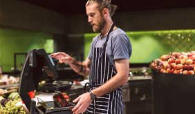 Young seller in apron thoughtfully weighing strawberries on digital scales in modern supermarket